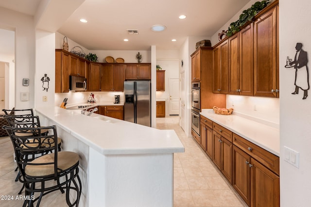 kitchen featuring a breakfast bar, sink, light tile patterned flooring, kitchen peninsula, and stainless steel appliances