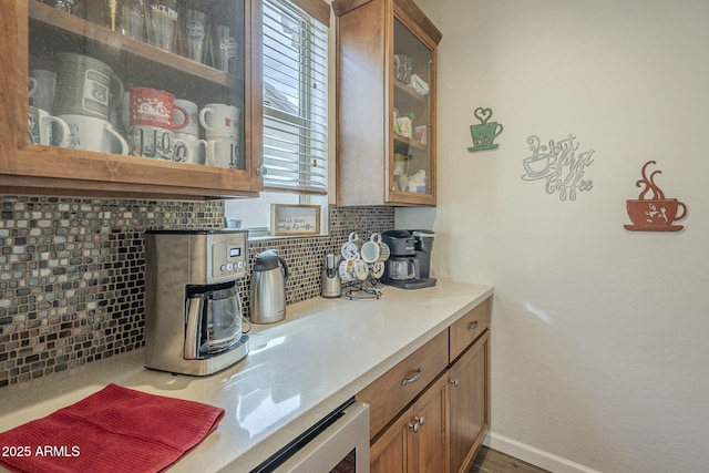 kitchen featuring brown cabinets, light countertops, backsplash, glass insert cabinets, and baseboards