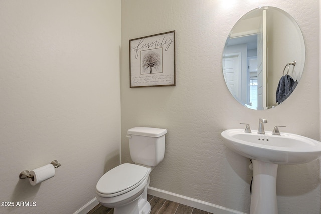 half bath featuring baseboards, a textured wall, toilet, and wood finished floors