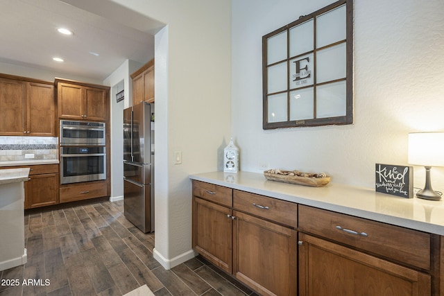 kitchen featuring light countertops, appliances with stainless steel finishes, decorative backsplash, brown cabinets, and dark wood finished floors