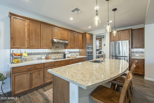 kitchen with brown cabinets, under cabinet range hood, appliances with stainless steel finishes, and dark wood finished floors