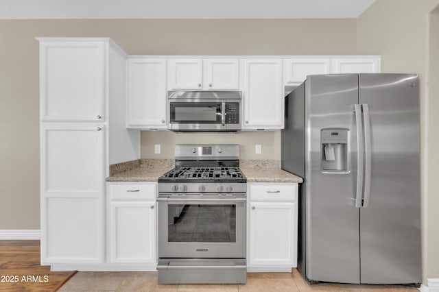 kitchen with stainless steel appliances, white cabinets, light stone countertops, and baseboards
