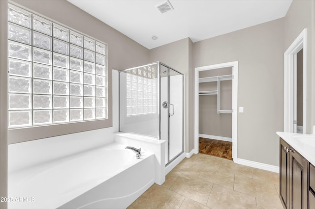 full bathroom with a shower stall, a bath, a walk in closet, baseboards, and vanity