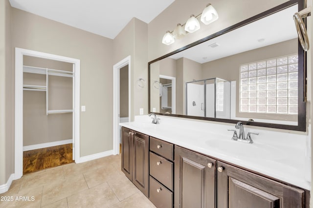 full bathroom featuring a shower stall, double vanity, a walk in closet, and baseboards