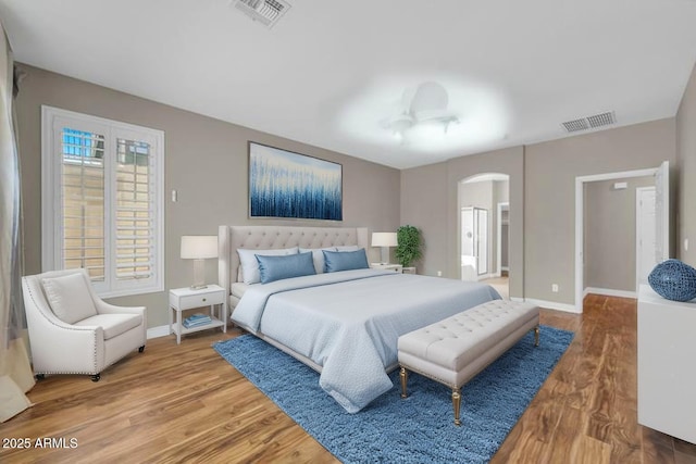 bedroom with arched walkways, wood finished floors, and baseboards