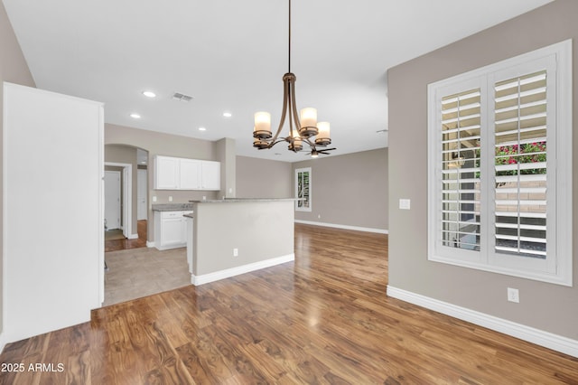 kitchen featuring a chandelier, white cabinets, arched walkways, light countertops, and light wood-style floors