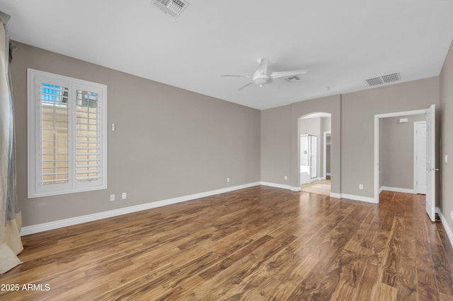 unfurnished room featuring arched walkways, a ceiling fan, wood finished floors, and baseboards