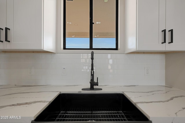 interior details featuring light stone counters, white cabinets, a sink, and decorative backsplash