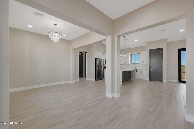 unfurnished living room featuring a chandelier, light wood-style flooring, a sink, visible vents, and baseboards