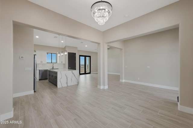 unfurnished living room with baseboards, light wood-style floors, a sink, and an inviting chandelier