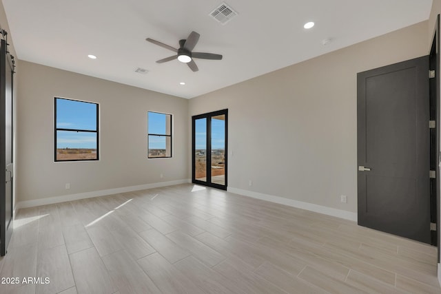 spare room with a barn door, recessed lighting, visible vents, baseboards, and a ceiling fan