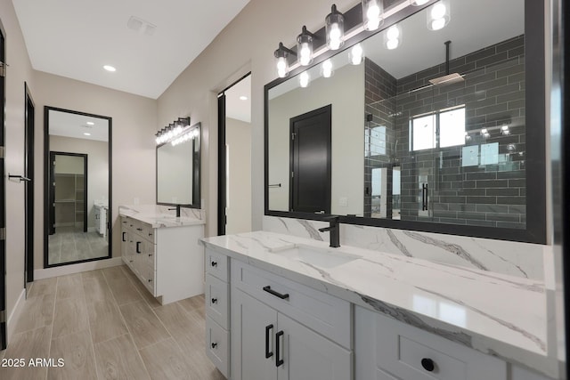 bathroom featuring a stall shower, wood tiled floor, two vanities, and a sink