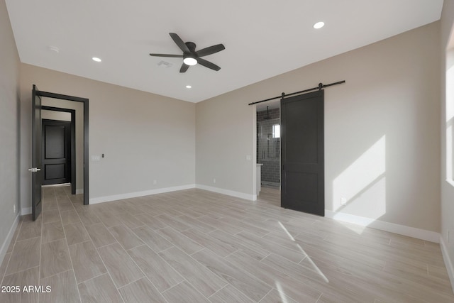 spare room with a ceiling fan, wood tiled floor, baseboards, and a barn door