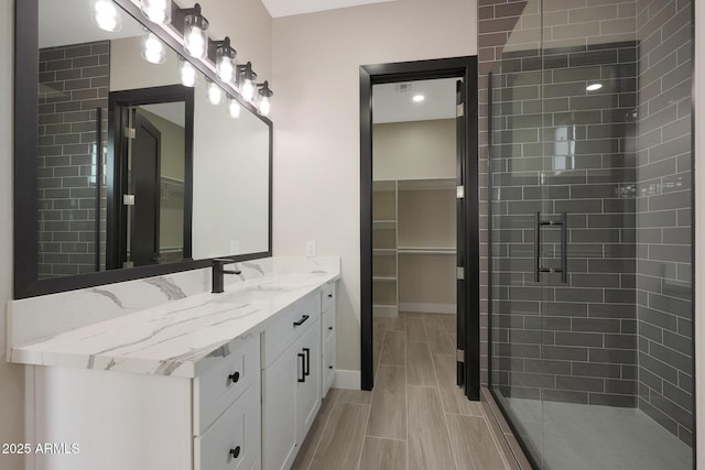 bathroom featuring wood finish floors, a spacious closet, a shower stall, vanity, and baseboards