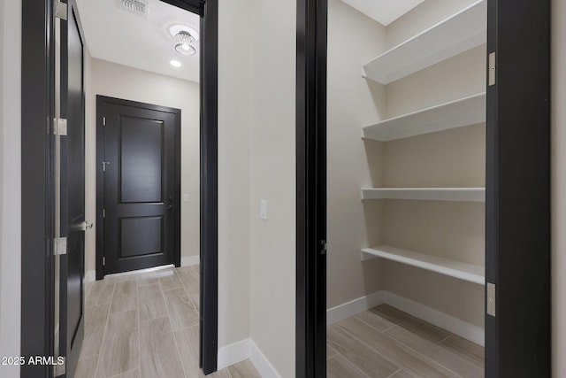 hall featuring wood tiled floor, visible vents, and baseboards