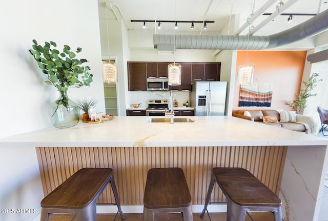 kitchen featuring sink, dark brown cabinets, appliances with stainless steel finishes, a kitchen breakfast bar, and kitchen peninsula