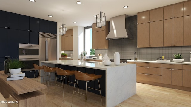 kitchen with a kitchen island with sink, tasteful backsplash, wall chimney range hood, and decorative light fixtures