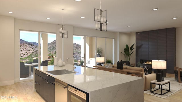 kitchen featuring hanging light fixtures, a fireplace, light hardwood / wood-style flooring, a center island with sink, and sink