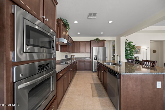 2163 N 164th Dr, Goodyear, AZ 85395 - kitchen with stainless steel appliances, dark stone counters, a kitchen island with sink, light tile patterned floors, and recessed lighting