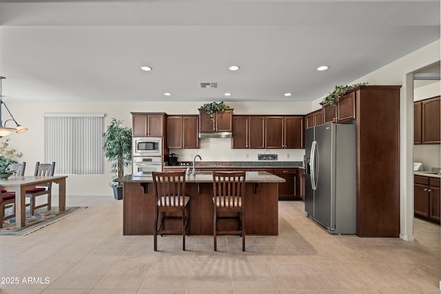 2163 N 164th Dr, Goodyear, AZ 85395 - kitchen featuring appliances with stainless steel finishes, under cabinet range hood, a kitchen bar, light stone counters, and recessed lighting