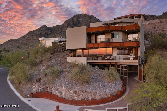 back house at dusk with a mountain view and a balcony