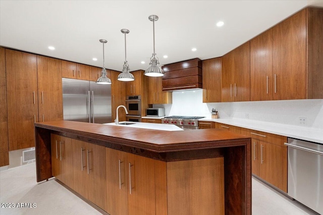 kitchen featuring pendant lighting, custom exhaust hood, sink, an island with sink, and appliances with stainless steel finishes