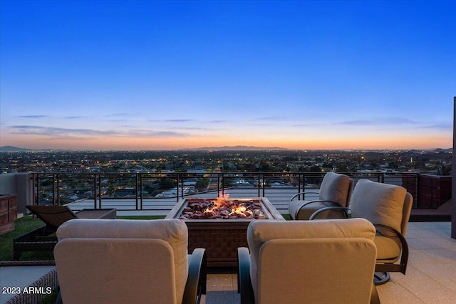 patio terrace at dusk featuring an outdoor fire pit and a balcony