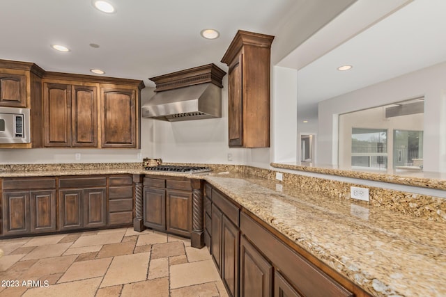 kitchen with light stone counters, wall chimney range hood, and stainless steel appliances