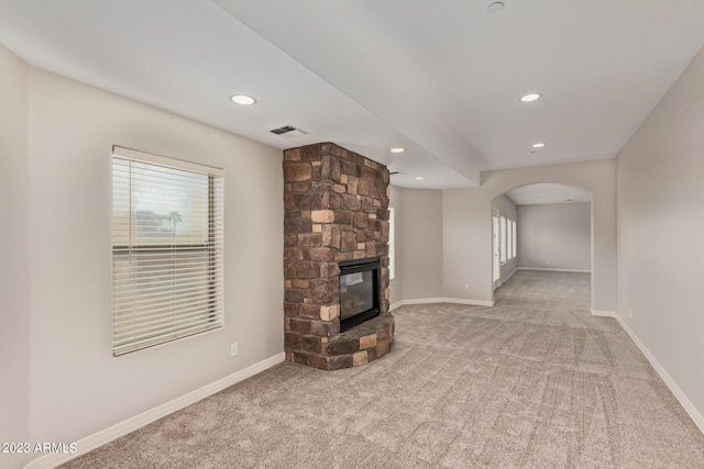 unfurnished living room featuring plenty of natural light, a stone fireplace, and light carpet