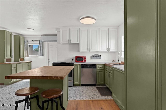 kitchen with green cabinetry, appliances with stainless steel finishes, a wall mounted air conditioner, butcher block countertops, and a kitchen bar