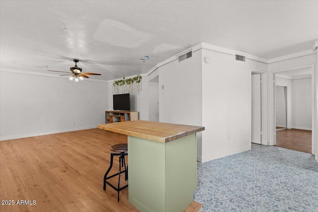 kitchen featuring ceiling fan, wood counters, a breakfast bar area, baseboards, and ornamental molding