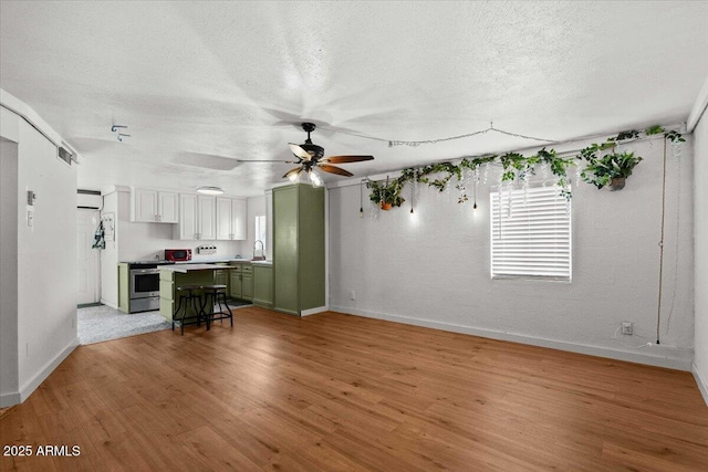living area with baseboards, light wood-style flooring, a textured ceiling, and a ceiling fan