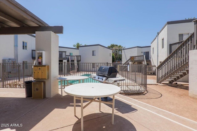 view of patio featuring fence, stairs, a community pool, and a residential view
