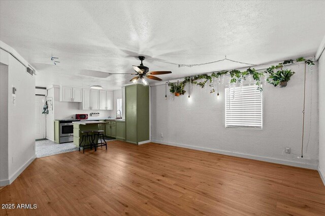 living area with baseboards, light wood-style flooring, a textured ceiling, and a ceiling fan