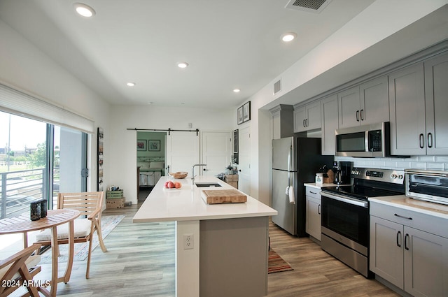 kitchen featuring a barn door, stainless steel appliances, sink, gray cabinets, and an island with sink