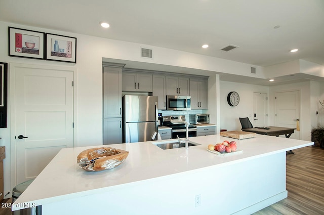 kitchen with tasteful backsplash, light hardwood / wood-style flooring, stainless steel appliances, gray cabinetry, and a large island