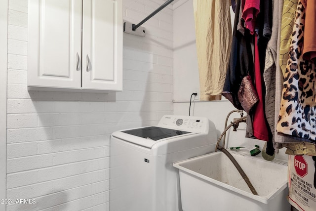 washroom with concrete block wall, cabinet space, washer / clothes dryer, and a sink