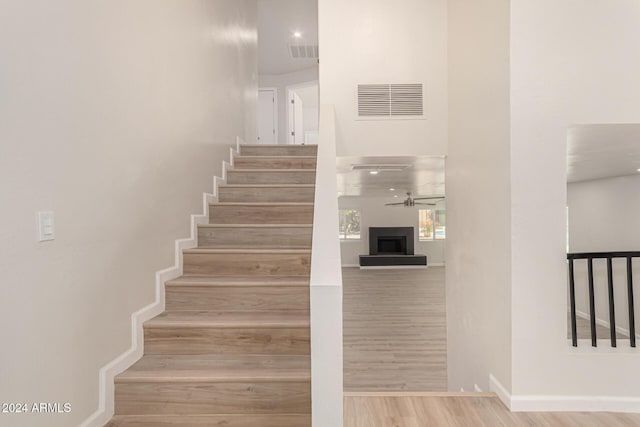 stairway featuring a fireplace with raised hearth, wood finished floors, visible vents, and baseboards