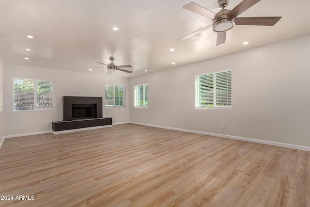 unfurnished living room with a fireplace with raised hearth, recessed lighting, baseboards, and light wood-style floors