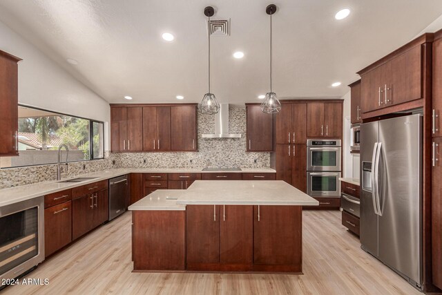 kitchen featuring appliances with stainless steel finishes, wall chimney exhaust hood, vaulted ceiling, pendant lighting, and light hardwood / wood-style flooring