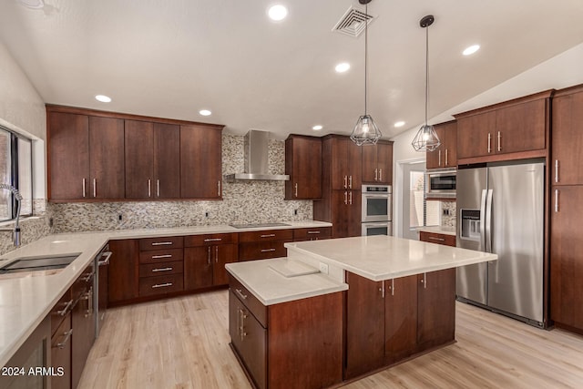 kitchen with a center island, light countertops, appliances with stainless steel finishes, a sink, and wall chimney exhaust hood