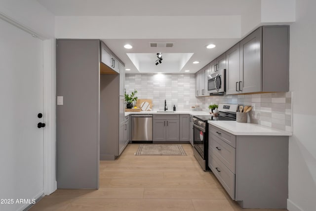 kitchen with visible vents, a raised ceiling, stainless steel appliances, gray cabinetry, and light wood-style floors