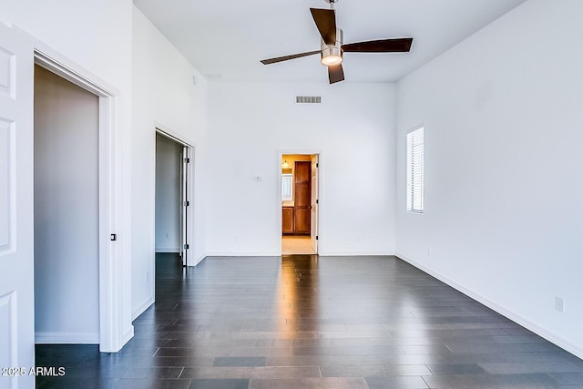 unfurnished room with ceiling fan, visible vents, dark wood finished floors, and baseboards