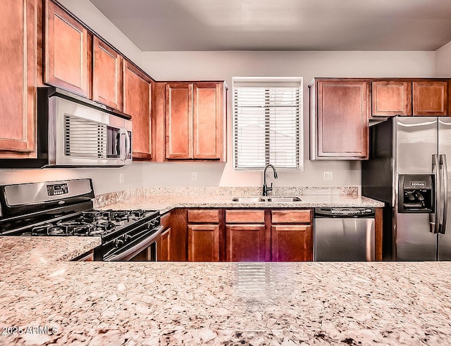 kitchen with appliances with stainless steel finishes, a sink, light stone counters, and brown cabinets