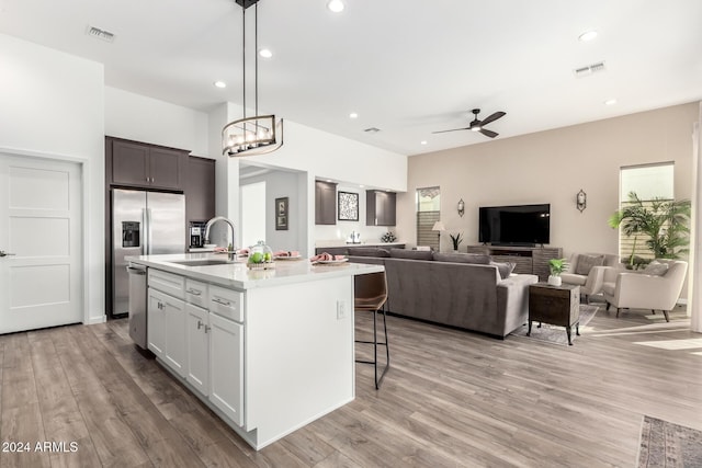 kitchen with a kitchen island with sink, ceiling fan with notable chandelier, sink, light hardwood / wood-style flooring, and decorative light fixtures