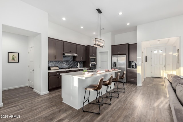 kitchen with a kitchen breakfast bar, dark brown cabinets, stainless steel appliances, dark wood-type flooring, and a center island with sink