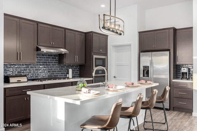 kitchen featuring sink, hanging light fixtures, stainless steel appliances, light hardwood / wood-style flooring, and an island with sink