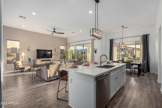 kitchen with stainless steel dishwasher, ceiling fan with notable chandelier, sink, hanging light fixtures, and an island with sink