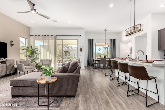 living room with ceiling fan with notable chandelier, light hardwood / wood-style flooring, and sink