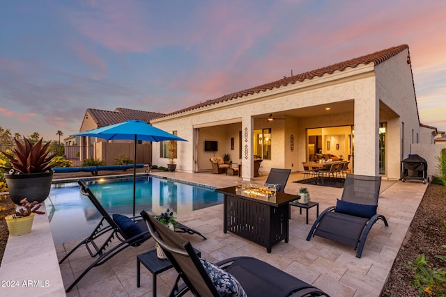 pool at dusk featuring a jacuzzi, a patio, a fire pit, and ceiling fan